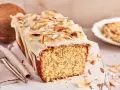 Saftiger Kuchen mit Kokosmilch, überzogen mit weißer Glasur und garniert mit gerösteten Kokoschips. Daneben eine Kokosnuss.