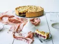 Ein saftiger Kirschkuchen mit Pudding und Streuseln auf einem Tortenständer. Ein Stück ist bereits auf einem Teller angerichtet.
