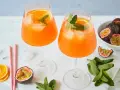 Zwei erfrischende Maracuja Spritz Cocktails mit Eis, Orangenscheiben und Minze, garniert mit frischen Passionsfrüchten.