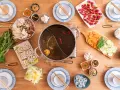 Zutaten für ein köstliches Hot Pot selber machen: Fleisch, Pilze, Gemüse, Garnelen und verschiedene Dips auf einem Holztisch arrangiert.