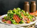 Warmer Rucolasalat mit knusprigem Speck, gerösteten Zwiebeln und Sonnenblumenkernen. Ein köstliches Gericht für Rucola Rezepte warm.