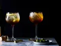Zwei erfrischende Cynar Spritz Cocktails mit Eis, Zitrone und Oliven, daneben eine Champagnerflasche.