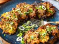 Knusprige Zucchini Kartoffel Puffer, garniert mit frischen Kräutern und Frühlingszwiebeln, liegen auf einem blauen Teller. Eine Gabel liegt daneben.