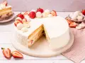 Eine köstliche Erdbeer Raffaello Torte, verziert mit frischen Erdbeeren und Raffaello Kugeln, auf einem Marmorsockel.