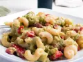 Cremiger nudelsalat mit avocado, Tomaten und Gewürzen auf einem weißen Teller.