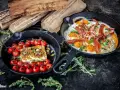 Zwei Gusseisenpfannen mit Eiern, Speck und Kirschtomaten mit Feta – perfekt für low carb grillen.