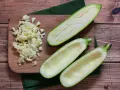 Vorbereitung für gefüllte Zucchini: ausgehöhlte Zucchinihälften und gehackter Knoblauch liegen bereit. Die Zucchini kerne essbar, werden oft mitverwendet.
