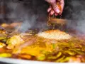 Gewürze werden über Reis und Gemüse gestreut, was zeigt, was ist paella: ein köstliches spanisches Reisgericht, das in einer großen Pfanne gekocht wird.