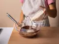 Eine Person gibt Amaranth zu geschmolzener Schokolade in einer Schüssel. Was ist Amaranth? Ein gesundes Getreide für leckere Rezepte.
