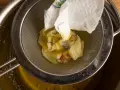 Ein Sieb hält ein Stück Papier mit Blumenmuster, das über einem Topf mit geschmolzener Butter liegt. Perfekt für raffinierte Butter Rezepte.