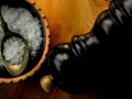 Fleur de sel, zarten Salzkristallen auf einem Löffel in einer Schale, neben einer dunklen Pfeffermühle.