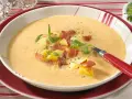 Eine dampfende, cremige Kartoffelsuppe mit Sahne, garniert mit Kartoffelwürfeln, knusprigem Speck und frischen Kräutern.