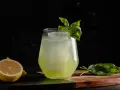 Erfrischender Basil Smash mit Zitrone und Basilikum garniert, serviert auf einem Holzbrett.
