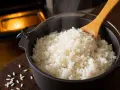 Dampfender Reis im Ofen gekocht, bereit zum Servieren. Ein Holzlöffel ragt aus dem Topf.