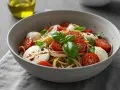 Spaghettisalat mit Knoblauch, Kirschtomaten und Mozzarella-Kugeln, garniert mit Basilikum. Ein leichter Genuss.