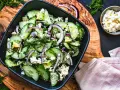 Erfrischender gurken feta salat mit Avocado, roten Zwiebeln und Dill, serviert in einer schwarzen Schüssel auf einem Holzbrett.