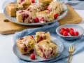Saftiger Kuchen mit Himbeeren, auf Tellern und einer Platte angerichtet, daneben eine Schale mit frischen Himbeeren.