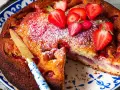 Saftiger Erdbeer Joghurt Kuchen, bestäubt mit Puderzucker und garniert mit frischen Erdbeeren. Ein Stück ist bereits angeschnitten.