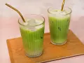 Zwei erfrischende Iced Matcha Latte mit goldenen Strohhalmen auf einem Holztablett. Perfekt für ein schnelles iced matcha latte rezept.