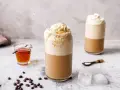 Eiskaffee selbst machen: Ein erfrischender Eiskaffee mit Sahne und Sirup, daneben Kaffeebohnen und Eiswürfel.