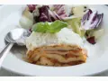 Ein Stück Lasagne mit Schmand, garniert mit Basilikum und Parmesan, serviert mit einem Salat.