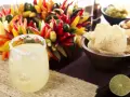 Ein erfrischendes Margarita-Rezept: Ein Glas mit Salzrand, Eiswürfeln und Limette, daneben bunte Chilis, Guacamole und Tortilla-Chips.