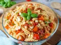 Ein köstlicher mediterraner Nudelsalat mit Fusilli, Kirschtomaten, Mozzarella und Basilikum, garniert mit frischen Basilikumblättern.