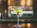 Ein klassischer Martini, perfekt für Ihr Martini Rezept. Mit Zitronenzeste garniert, steht er auf einer Holztheke.