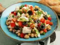 Ein bunter Kichererbsen Thunfisch Salat mit Paprika, Oliven und Petersilie, appetitlich auf einem blauen Teller angerichtet.