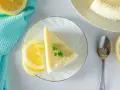Ein Stück Philadelphia Torte Zitrone, garniert mit Minze und Kokosraspeln, neben Zitronenscheiben und einem Löffel.
