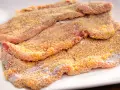 Mehrere rohe Schnitzel liegen auf einem weißen Teller, bereit zum Schnitzel panieren. Die Panade ist goldbraun und knusprig.