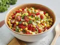 Bunter Paprika Mais Salat mit Tomaten, Zwiebeln und Kräutern in einer Schüssel.