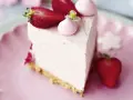 Ein Stück Erdbeer Cheesecake ohne Backen, dekoriert mit frischen Erdbeeren und rosa Baiser-Tupfern auf einem rosa Teller.