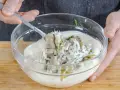 Matjes Hausfrauenart, Omas Rezept: Ein Löffel voll cremiger Sauce mit Matjesstücken und Dill wird aus einer Glasschüssel gehoben.