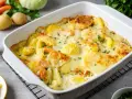Kartoffeln mal anders: Cremiger Kartoffelauflauf mit Möhren und Erbsen, überbacken mit Käse und garniert mit Petersilie.