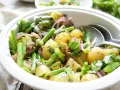 Frischer Kartoffel Bohnen Salat mit roten Zwiebeln und Kräutern in einer weißen Schüssel, bereit zum Servieren.