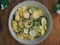 Ein Teller mit lauwarmer bayrischer Kartoffelsalat, garniert mit Radieschen, Gurken und Schnittlauch.