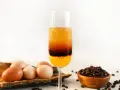 Schicht-Cocktail mit Ei, Kaffee und Orangensaft. Daneben liegen Eier und Kaffeebohnen.