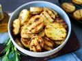 Schmackhafte Kartoffelscheiben mit Rosmarin, perfekt gegrillt. Die Streifen vom Grill sind deutlich sichtbar.
