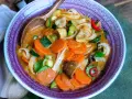 Eine dampfende, cremige Thai Curry Suppe mit Karotten, Zucchini, Pilzen und Reisnudeln in einer lila Schüssel.