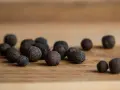 Eine Gruppe von Pimentkörnern liegt auf einem Holzbrett. Was ist Piment? Diese aromatischen Beeren duften nach Zimt, Nelken und Muskat.