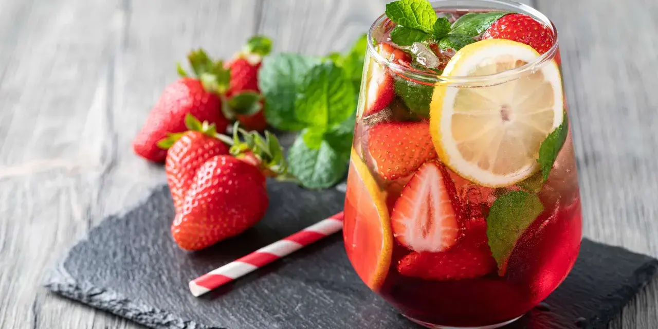 Erfrischende alkoholfreie Bowle mit Erdbeeren, Zitrone und Minze, serviert in einem Glas mit Eiswürfeln.