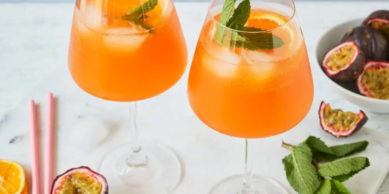 Zwei erfrischende Maracuja Spritz Cocktails mit Eis, Orangenscheiben und Minze, garniert mit frischen Passionsfrüchten.