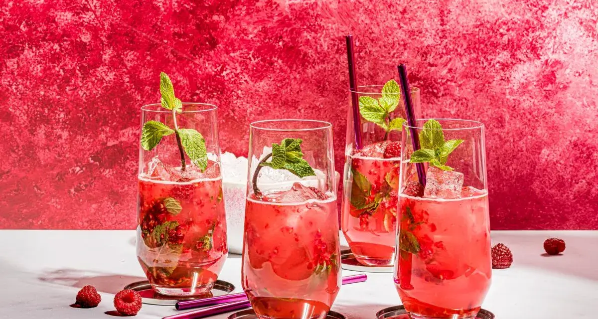 Vier erfrischende Bacardi Razz Mojitos mit Himbeeren und Minze, bereit zum Genießen.