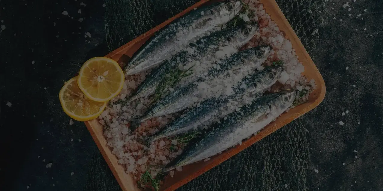 Frische Sardinen und Sardellen auf einem Holzbrett mit Zitrone und Kräutern, bereit für die Zubereitung. Der Unterschied zwischen Sardinen und Sardellen ist hier nicht ersichtlich.