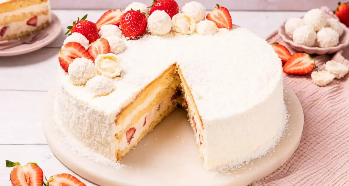 Eine köstliche Erdbeer Raffaello Torte, verziert mit frischen Erdbeeren und Raffaello Kugeln, auf einem Marmorsockel.