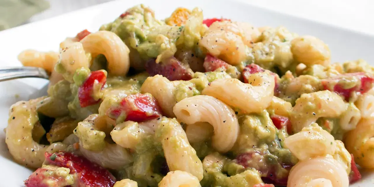 Cremiger nudelsalat mit avocado, Tomaten und Gewürzen auf einem weißen Teller.