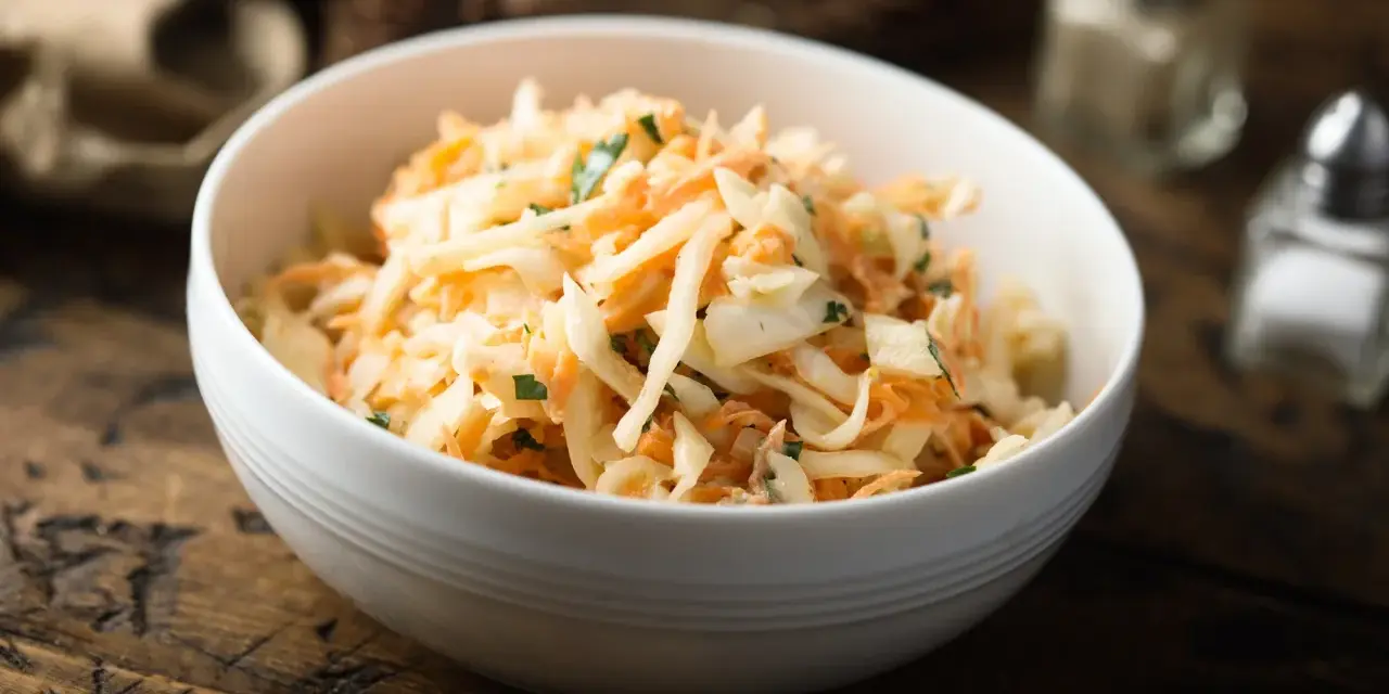 Schüssel mit cremigem Rettichsalat mit Apfel und Kräutern, serviert auf einem rustikalen Holztisch.