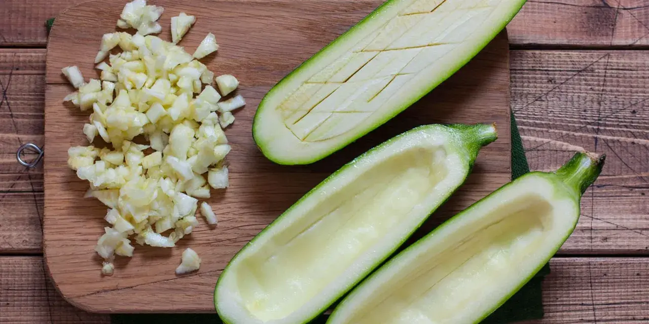 Vorbereitung für gefüllte Zucchini: ausgehöhlte Zucchinihälften und gehackter Knoblauch liegen bereit. Die Zucchini kerne essbar, werden oft mitverwendet.