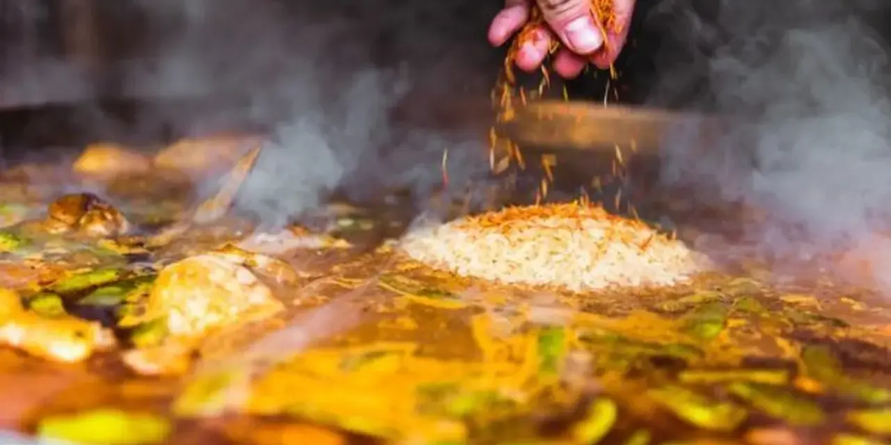 Gewürze werden über Reis und Gemüse gestreut, was zeigt, was ist paella: ein köstliches spanisches Reisgericht, das in einer großen Pfanne gekocht wird.